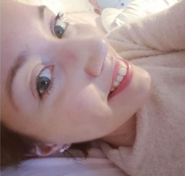 Ein lächelndes Gesicht mit geöffnetem Mund. Die Person liegt auf einem weichen, rosa Tuch.