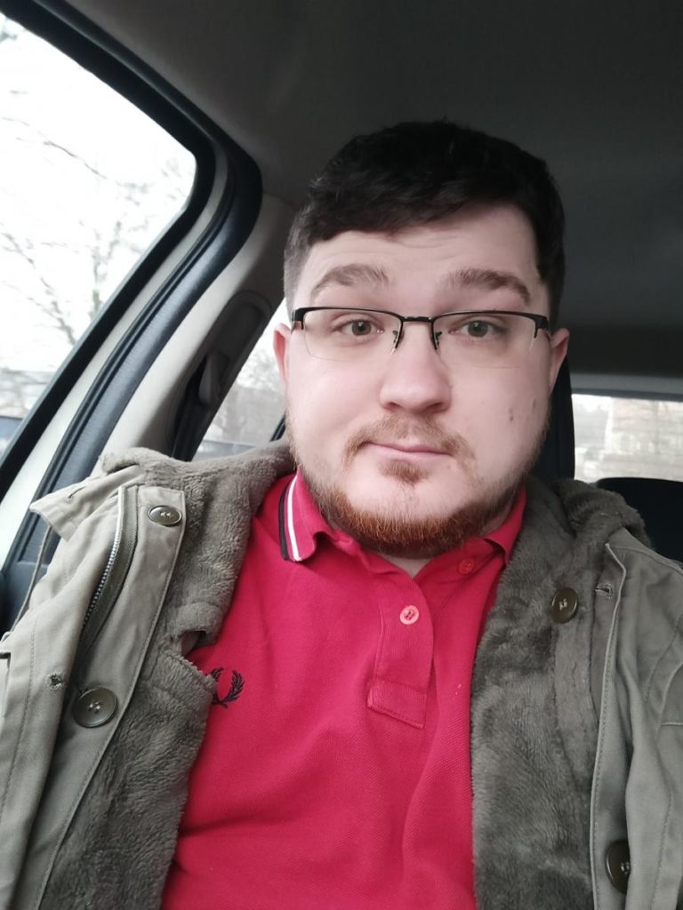 Ein junger Mann mit Brille und rotem Polohemd sitzt im Auto.