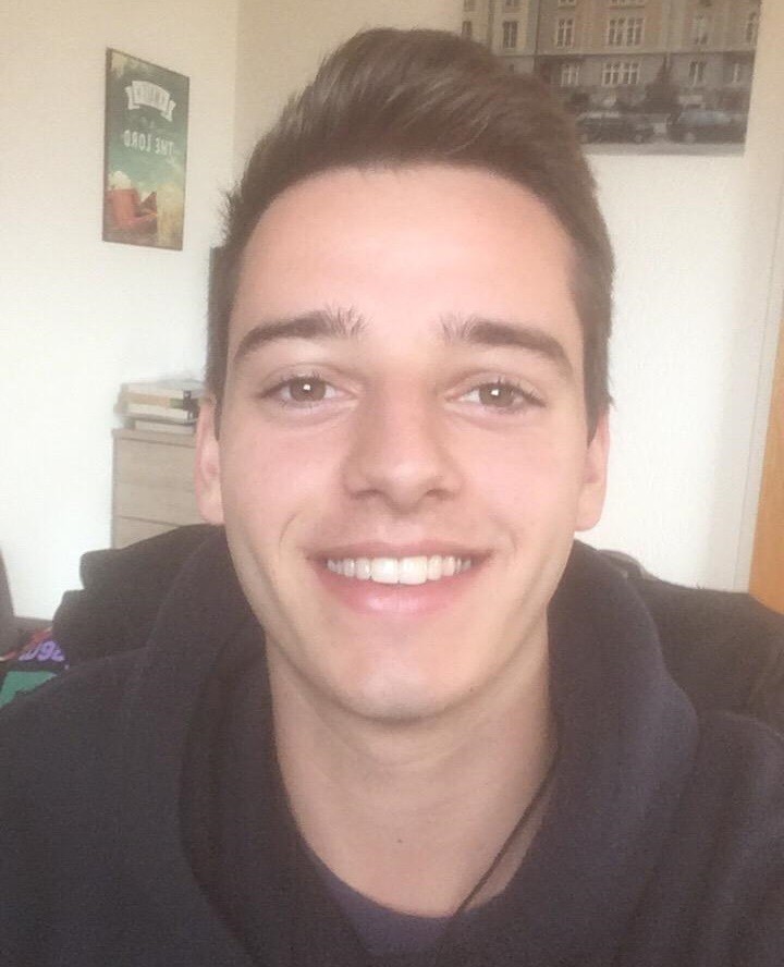 Ein junger Mann mit kurzen braunen Haaren lächelt freundlich. Er trägt ein dunkles Sweatshirt.