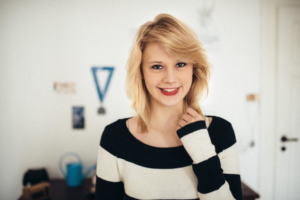 Eine junge Frau mit blondem Haar und einem schwarzen und weißen Pullover lächelt in die Kamera.