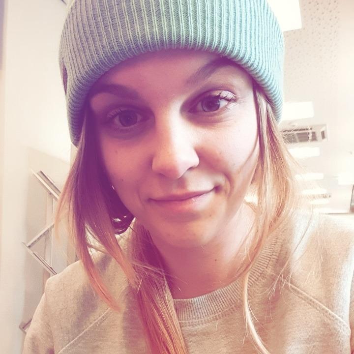 Eine junge Frau mit langen Haaren und einem freundlichen Lächeln, die einen Beanie und einen Pullover trägt.