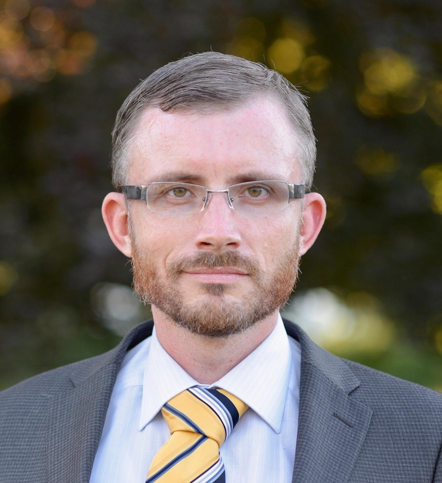 Ein Mann mit grauen Haaren, Brille und gelber Krawatte im Freien.