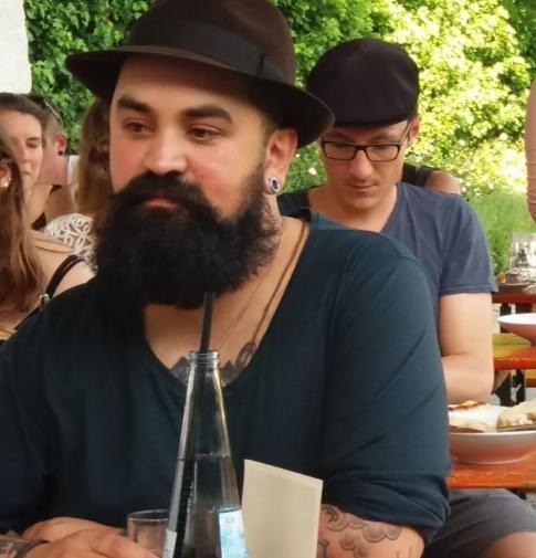 Ein Mann mit einem Bart und einem Hut sitzt im Restaurant und trinkt aus einer Flasche.