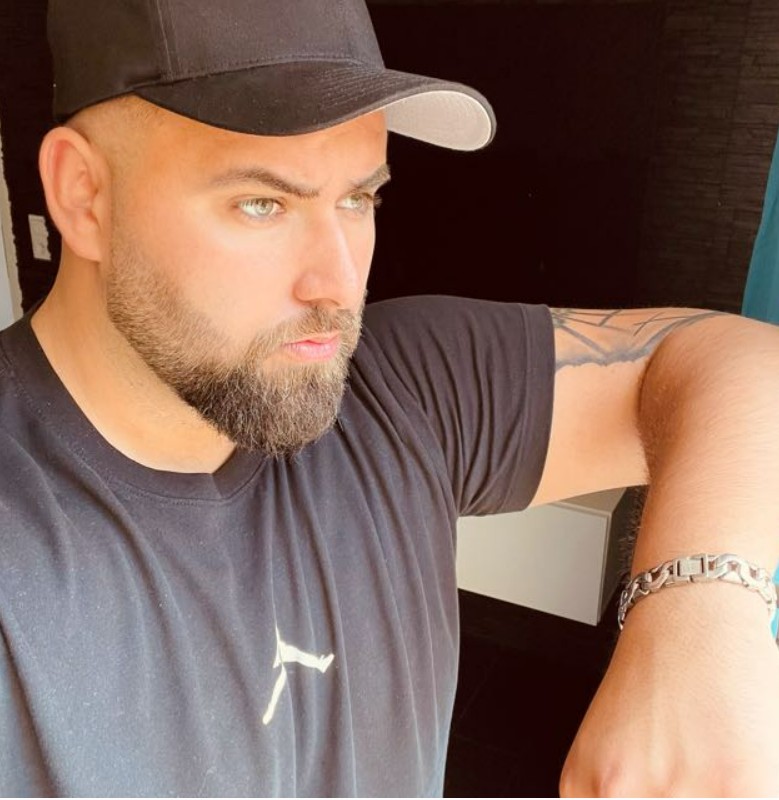 Ein Mann mit Bart und Baseballmütze, tätowierter Arm