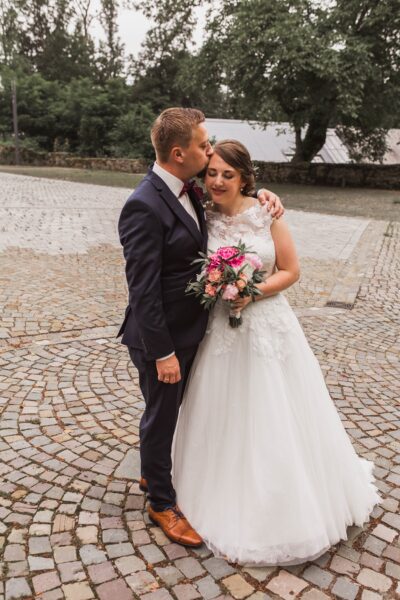 Ein Brautpaar in einer romantischen Umarmung. Die Braut trägt ein weiÐes Kleid und einen Blumenstrauße.