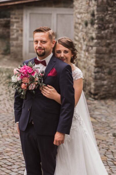 Ein frisch verheiratetes Paar posiert führ eine Hochzeitsfotografie. Die Braut trägt ein weiße Kleid und liegt in den Armen des Bräutigams.